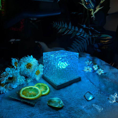 Crystal block glowing under blue light with flowers and fruit on a dark surface